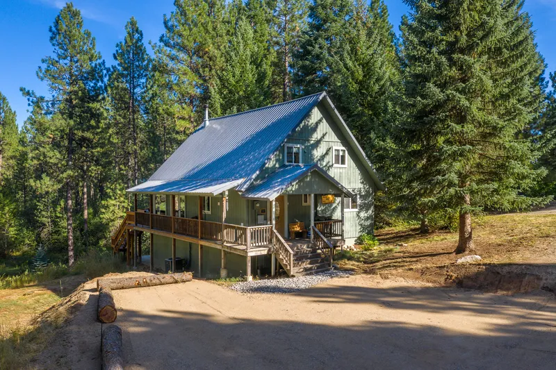 Aerial view of a mountain cabin in Garden Valley, Idaho, surrounded by pine trees, featuring a wraparound porch and rustic design—ideal for real estate and vacation rental marketing.