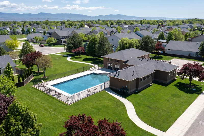 Aerial drone view of a residential community in Meridian, Idaho, featuring a swimming pool, clubhouse, green spaces, and a backdrop of the Treasure Valley mountains.