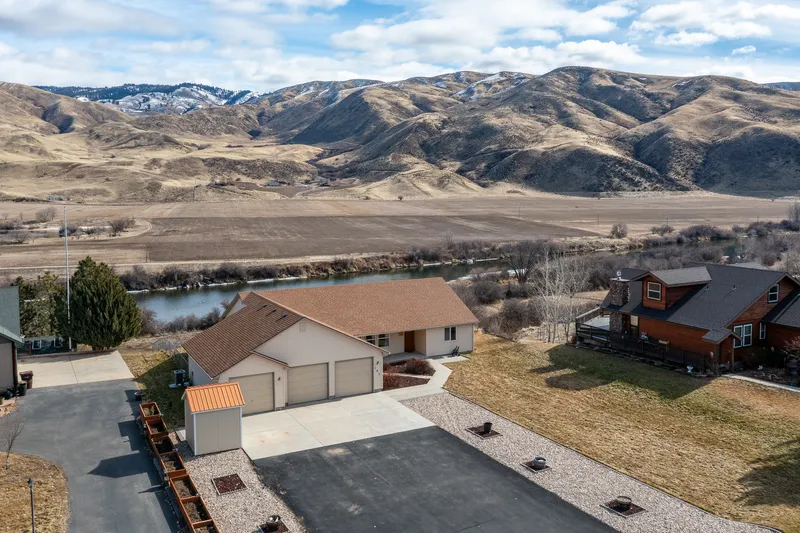 Aerial view of a home in Horseshoe Bend, Idaho, featuring panoramic mountain views, the Payette River, and a spacious residential property in a peaceful rural setting.