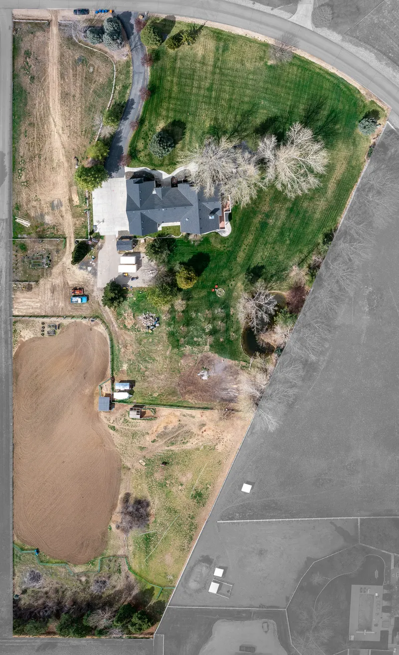 Aerial drone shot of a luxury acreage estate in Idaho, featuring a large custom home, extensive green space, farmland, and a private driveway.