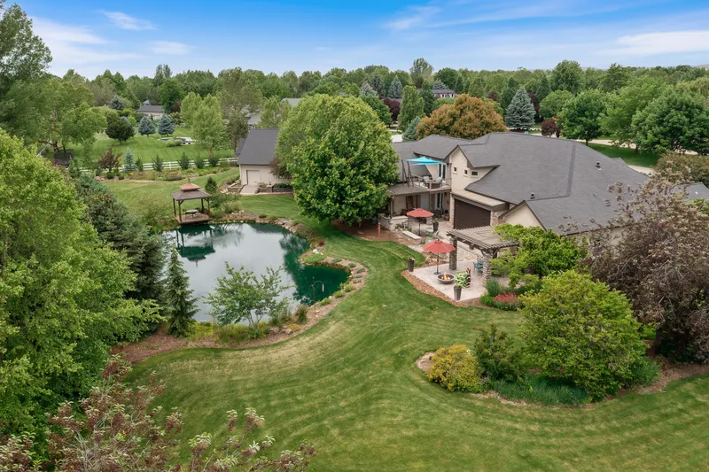Aerial drone view of a luxury estate in Eagle, Idaho, featuring a private pond, expansive yard, and multi-level patio, professionally captured for real estate marketing.