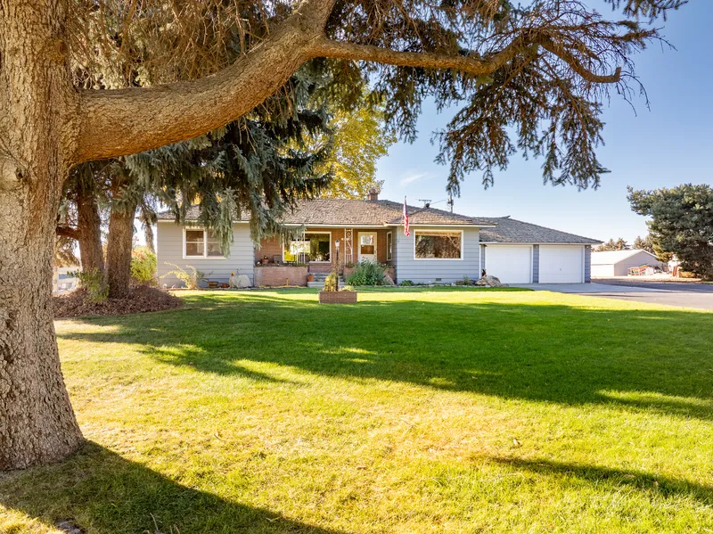 Aerial view of a rural Idaho home with large trees, well-manicured lawn, and a spacious driveway, captured using professional drone real estate photography.