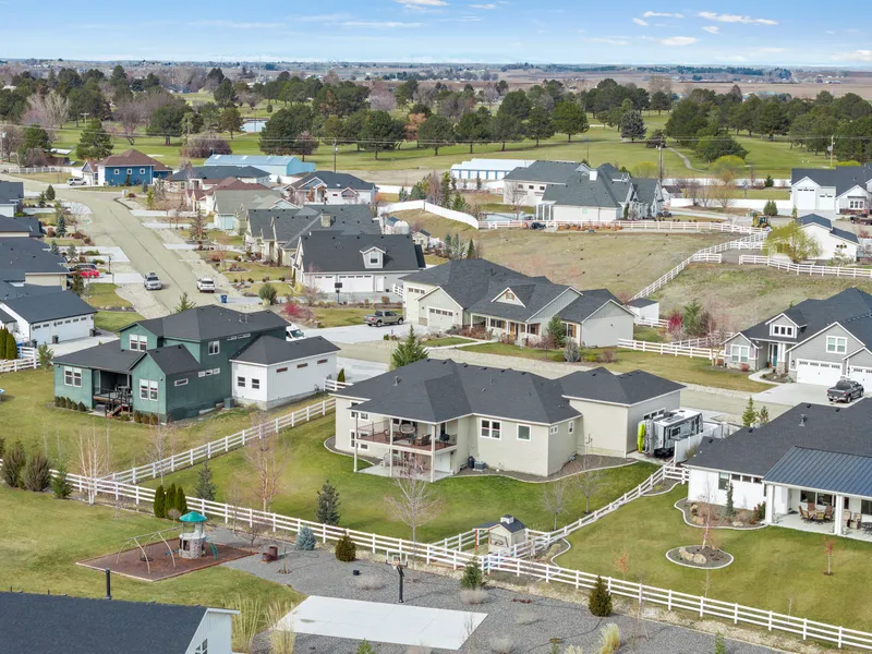 Aerial view of a suburban neighborhood in Caldwell, Idaho, featuring homes with large yards, white fencing, and a golf course in the background.