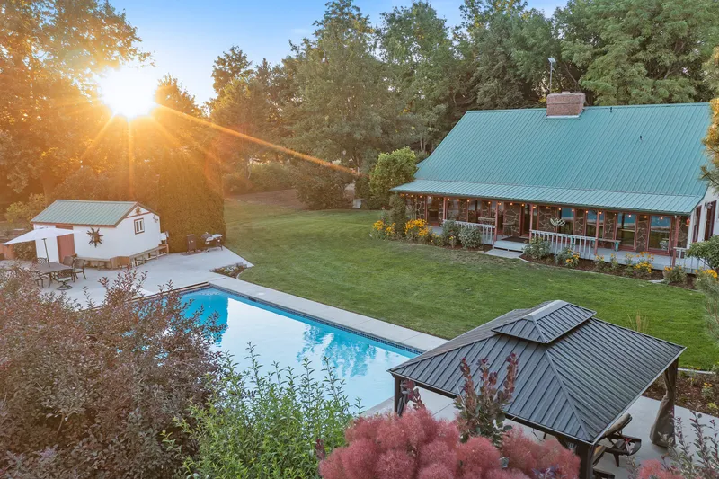 Elevated drone shot of a poolside property in Nampa, Idaho, with a sunset view, cabin-style home, and landscaped yard.