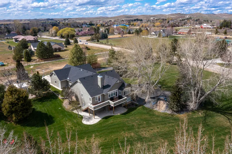 Aerial drone view of a luxury estate home in Eagle, Idaho, surrounded by mature trees, open land, and a scenic rural landscape.