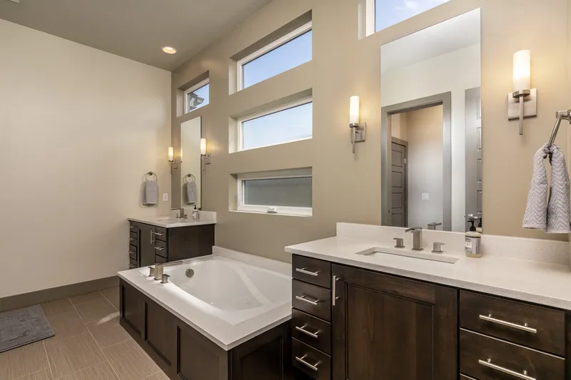 High-end Boise home bathroom with a deep soaking tub, dual vanities, modern lighting, and floor-to-ceiling windows, captured in professional real estate photography.