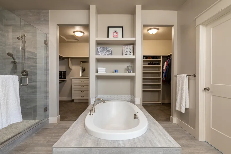 Luxury bathroom in Eagle home with a centered soaking tub, built-in shelving, spacious walk-in closets, and a glass-enclosed shower with floor-to-ceiling tile.