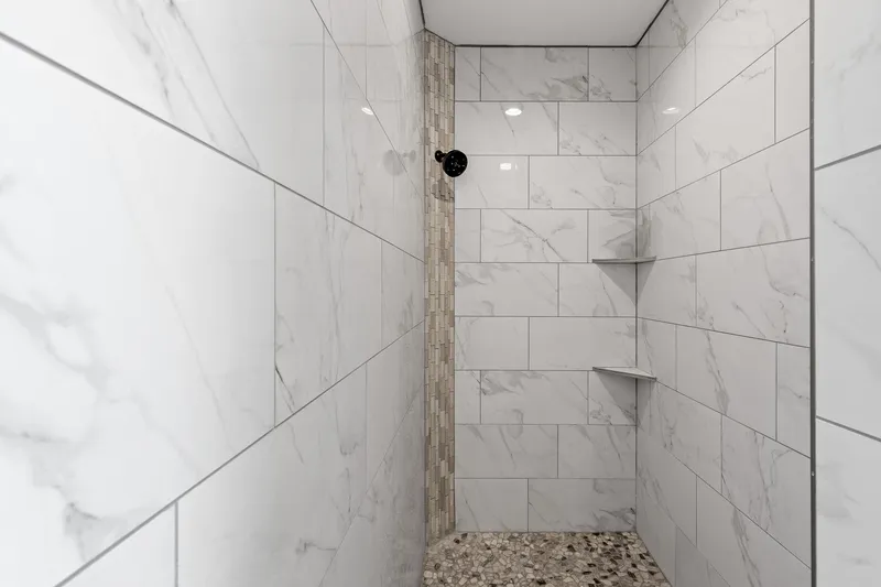 Modern tiled walk-in shower with marble-style walls and pebble flooring, featured in a professional real estate listing in Eagle, Idaho.