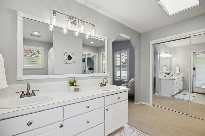 Elegant ensuite bathroom with double vanity, white cabinets, modern lighting, and a large mirrored closet in Avimor, Idaho, professionally photographed for real estate listings.