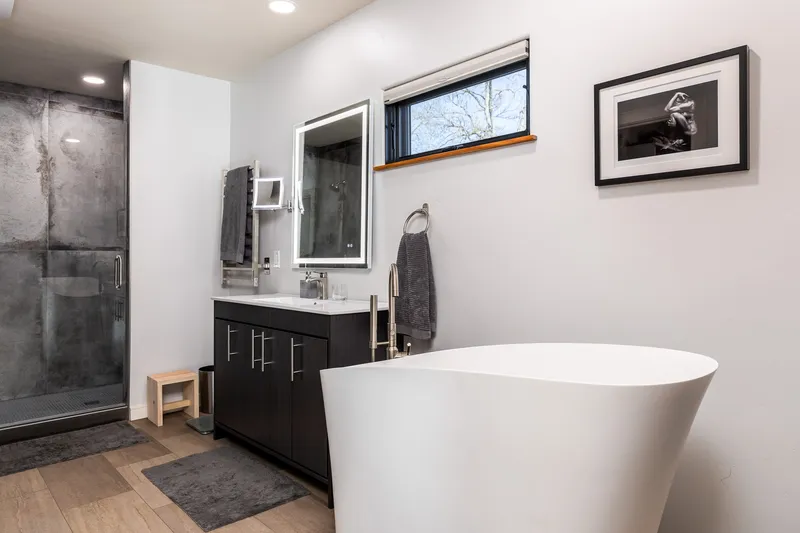 Modern bathroom in North End Boise featuring a white freestanding tub, LED vanity mirror, custom black cabinetry, and a concrete walk-in shower.