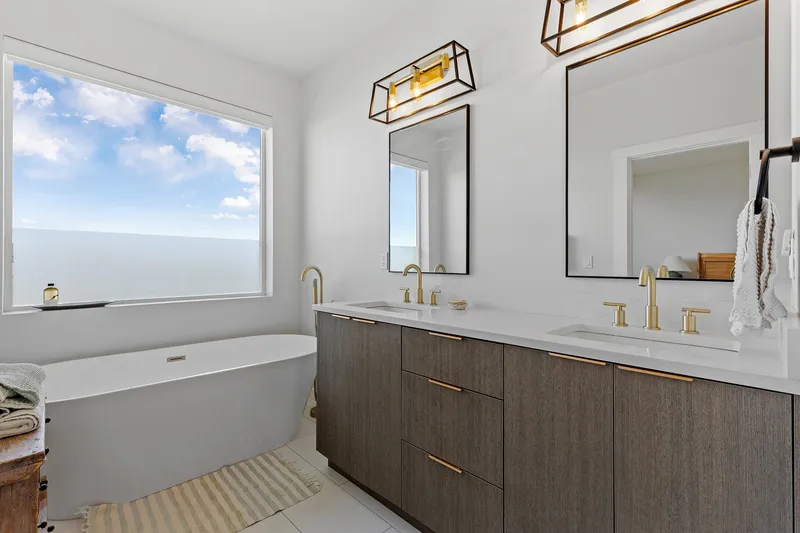 Luxury bathroom in Eagle, Idaho, featuring a freestanding soaking tub, double vanity with gold fixtures, and large windows, professionally photographed for real estate marketing.
