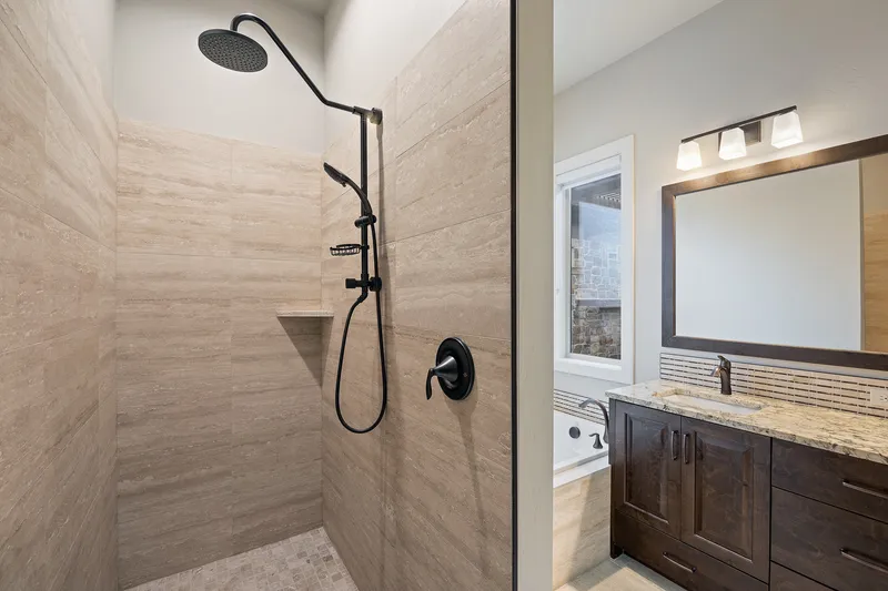 Luxury walk-in shower in Boise, Idaho, with natural stone tile, a rainfall showerhead, and bronze fixtures, professionally photographed for real estate marketing.