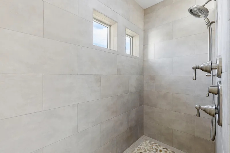 Luxury walk-in shower with large tile walls, pebble stone flooring, and dual showerheads in a modern Treasure Valley home.