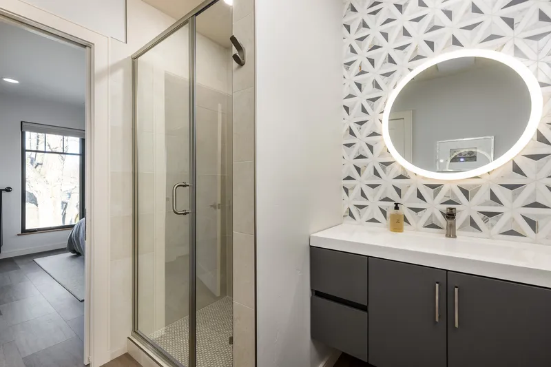 Modern bathroom design in North End Boise with a geometric tile backsplash, LED round mirror, floating vanity, and a glass-enclosed shower.