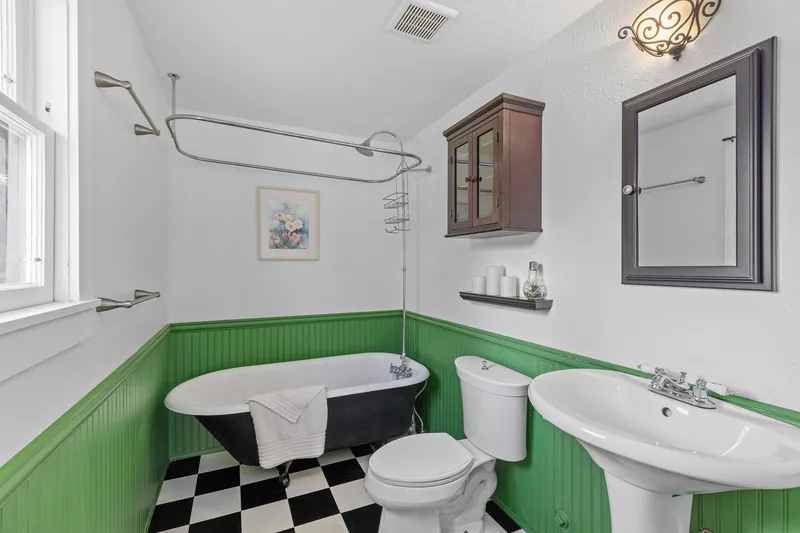 Vintage bathroom in Caldwell, Idaho, with a clawfoot tub, checkerboard tile flooring, and green wainscoting, professionally photographed for real estate listings.