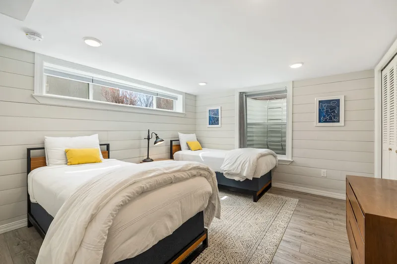 Bright basement bedroom in Boise, Idaho, with twin beds, shiplap walls, modern decor, large egress windows, and soft lighting.