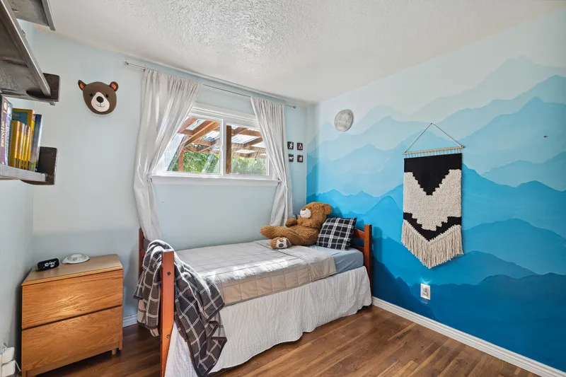 Boise bedroom with a blue mountain-themed accent wall, a twin bed, and natural light, ideal for real estate photography and home decor inspiration.