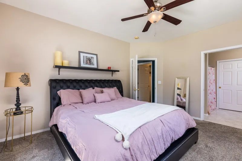 A modern Boise bedroom with a black tufted bed, soft pink bedding, a ceiling fan, and an en-suite bathroom.
