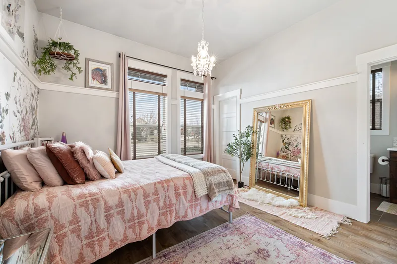 A stylish bedroom in Kuna, Idaho, featuring a plush bed with decorative pillows, a large gold-framed mirror, and soft natural light, captured for real estate marketing and interior design showcases.