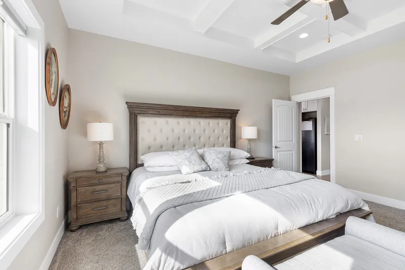 Luxury master bedroom with a tray ceiling, upholstered bed, and natural light in a modern Treasure Valley home.