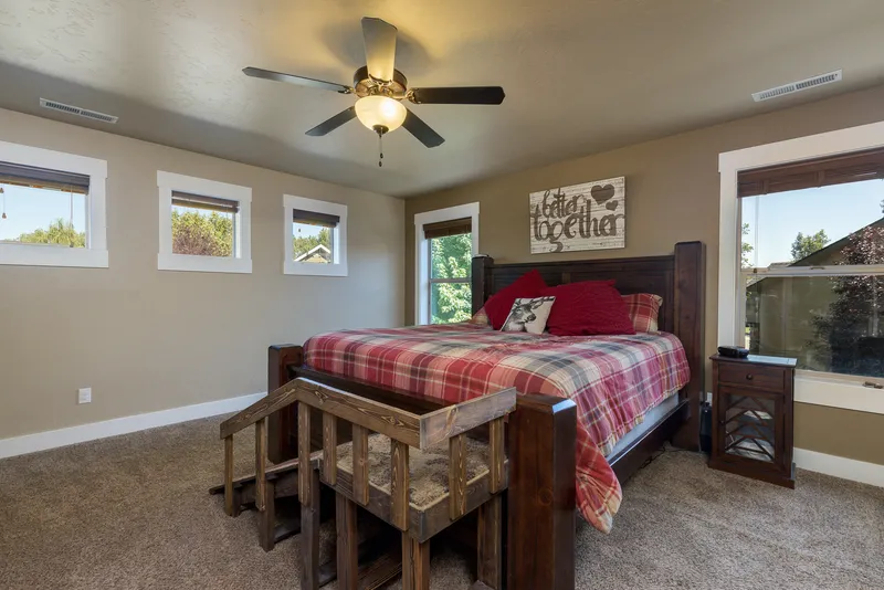 Master bedroom in a Meridian, Idaho home with rustic wooden bed frame, plaid bedding, and natural light from multiple windows.