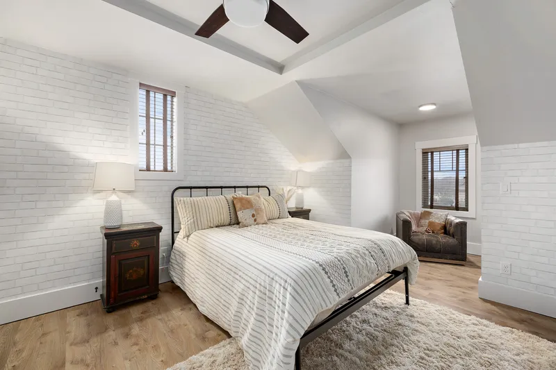 A modern bedroom in Meridian with a cozy bed, white brick accent walls, warm lighting, and a comfortable reading nook, photographed for real estate listing presentation.