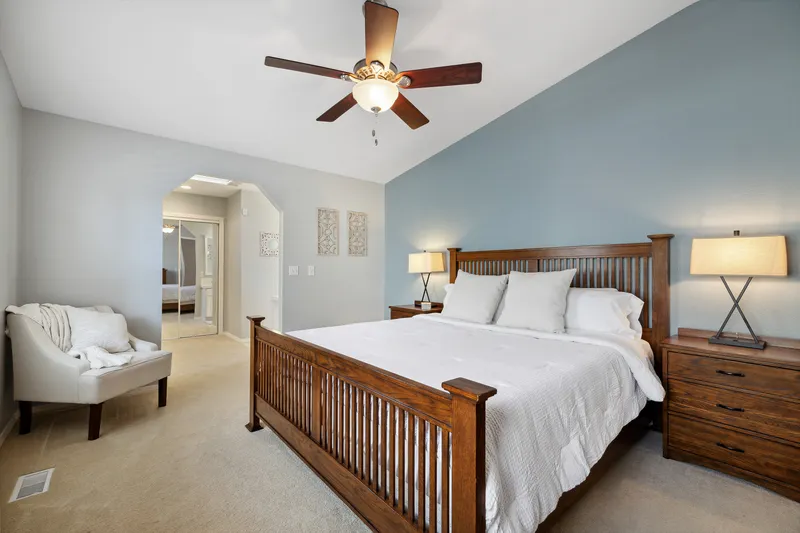 Serene primary bedroom with vaulted ceiling, rustic wood bed frame, and cozy seating area in Hidden Springs, Idaho, professionally photographed for real estate marketing.