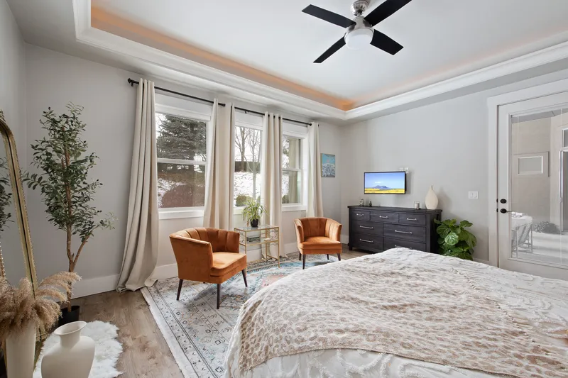 A modern, well-lit bedroom in Star, Idaho, featuring a plush bed, burnt-orange accent chairs, and large windows with scenic views, photographed for high-end real estate marketing.