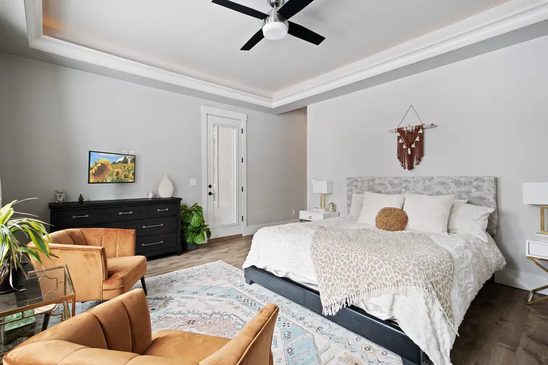 A modern master bedroom in Star, Idaho, featuring a plush king-sized bed, decorative pillows, accent chairs, and a sleek black dresser, photographed for high-end real estate listings.