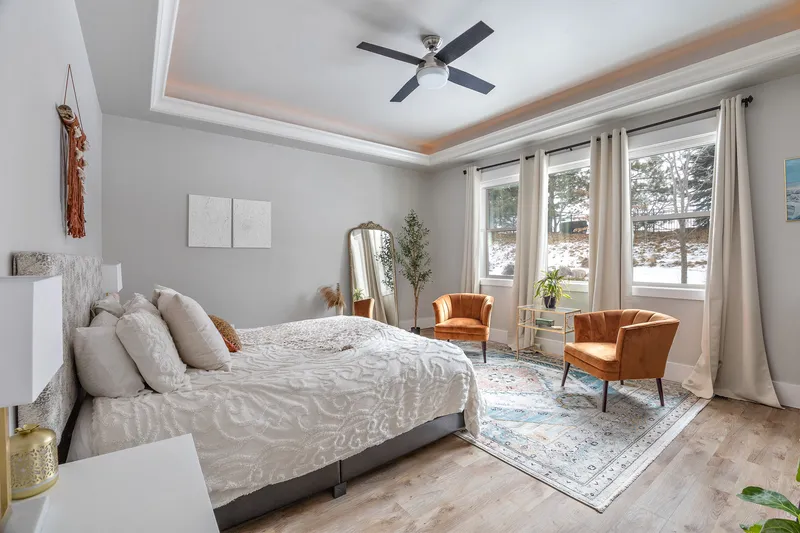 A modern bedroom in Star, Idaho, with a large bed, neutral-toned decor, accent chairs, and expansive windows, captured in high-quality real estate photography.