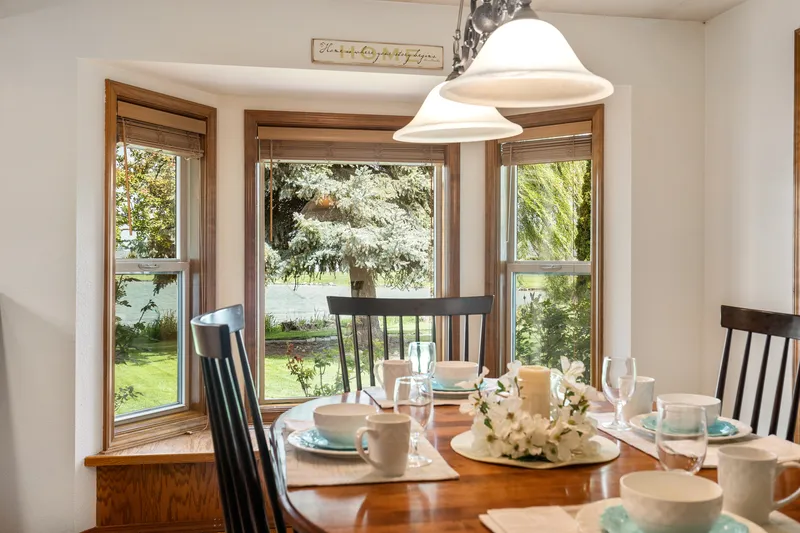 A sunlit dining area with bay windows, a wooden table set for a meal, and scenic outdoor views, ideal for real estate listing photography, home staging, and professional property marketing in Meridian.