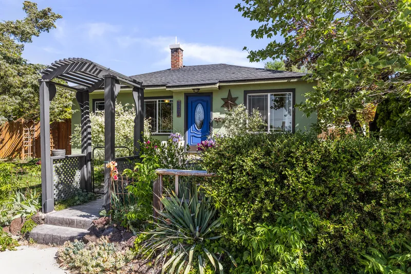 Garden City home with vibrant landscaping, an arched pergola entrance, and a welcoming blue door, ideal for real estate marketing, professional home photography, and listing promotions.