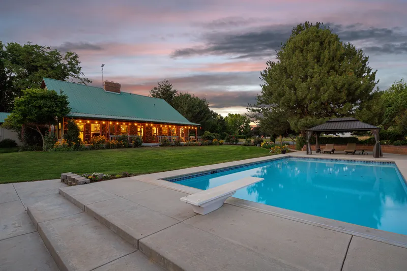 Twilight poolside view of a cabin-style home in Nampa, Idaho, with a sparkling pool, gazebo, and warm exterior lighting, professionally captured for real estate listings.