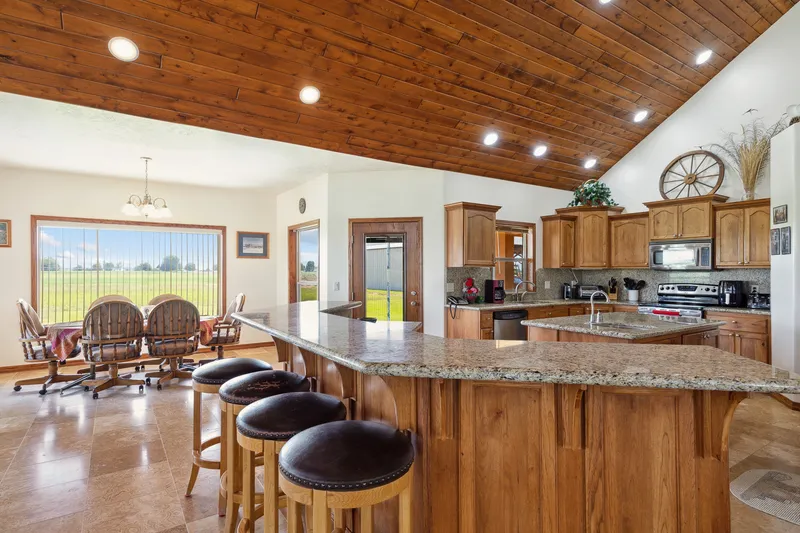 Rustic kitchen in a Caldwell home with vaulted wood ceilings, granite countertops, and a large island with barstools overlooking a scenic landscape.