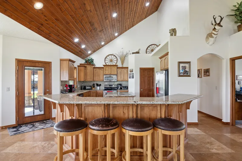 Rustic living room in a Caldwell home with a stone fireplace, vaulted wood ceiling, and large windows overlooking green fields.