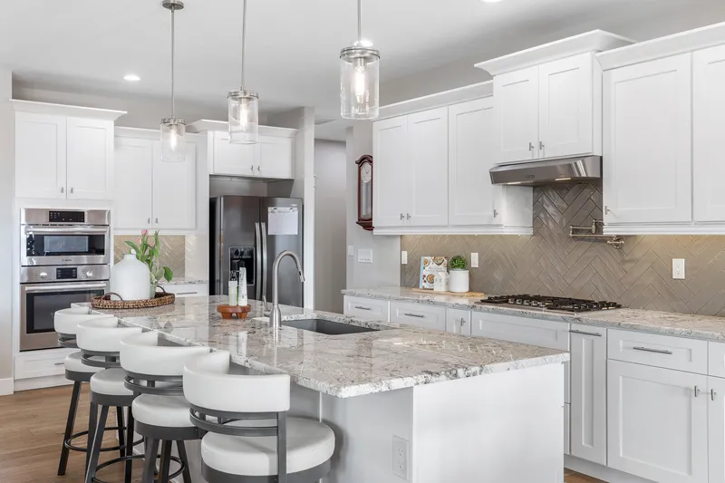 Luxury kitchen in a Treasure Valley home, featuring a large island with seating, white cabinetry, granite countertops, and a herringbone tile backsplash.